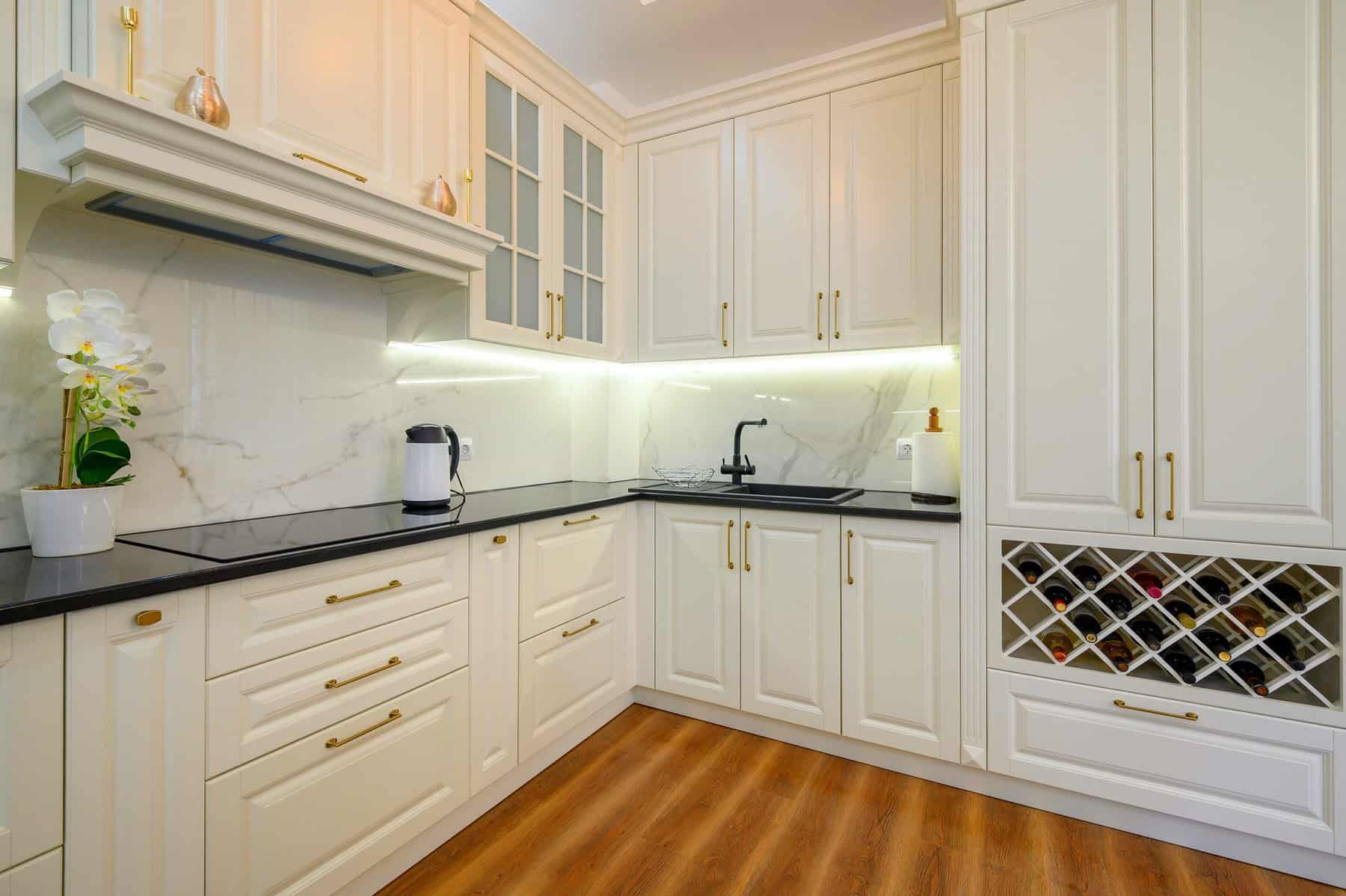 Elegant White Kitchen Cabinet Painting Elegant white kitchen cabinets with gold hardware, under cabinet lighting, and a built in wine rack.